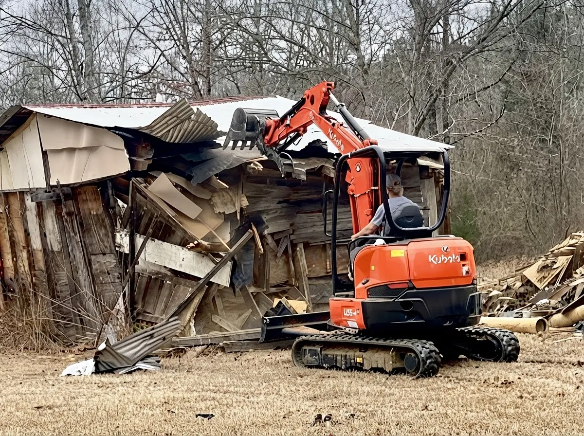 Excavator bucket taking down a wooden shed
